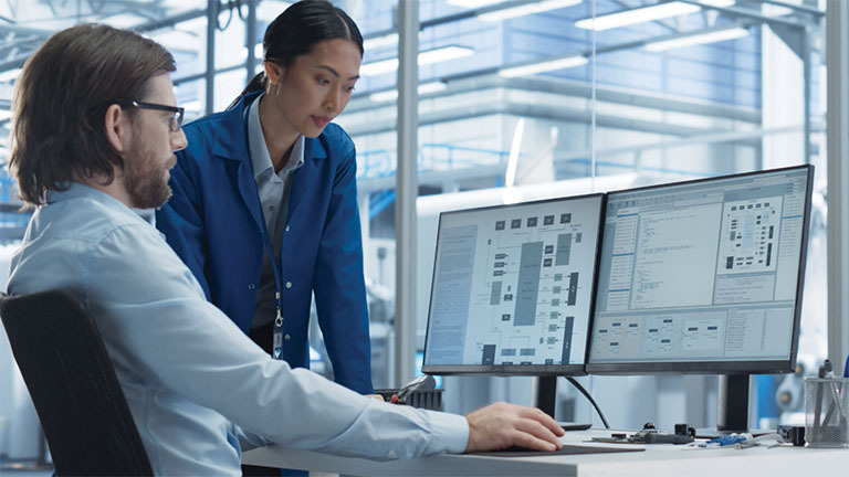 man and woman at desk looking at computer monitors